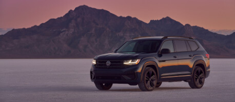 Black 2023 Volkswagen Atlas parked in empty desert field near mountains at sunrise