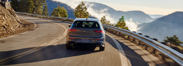 Grey 2023 Volkswagen Golf GTI driving on mountain side road with mountain vista