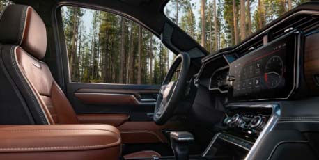 gmc_vehicle_front_passenger_interior_with_brown_leather_seats_and_infotainment_screen_with_forest_view_outside