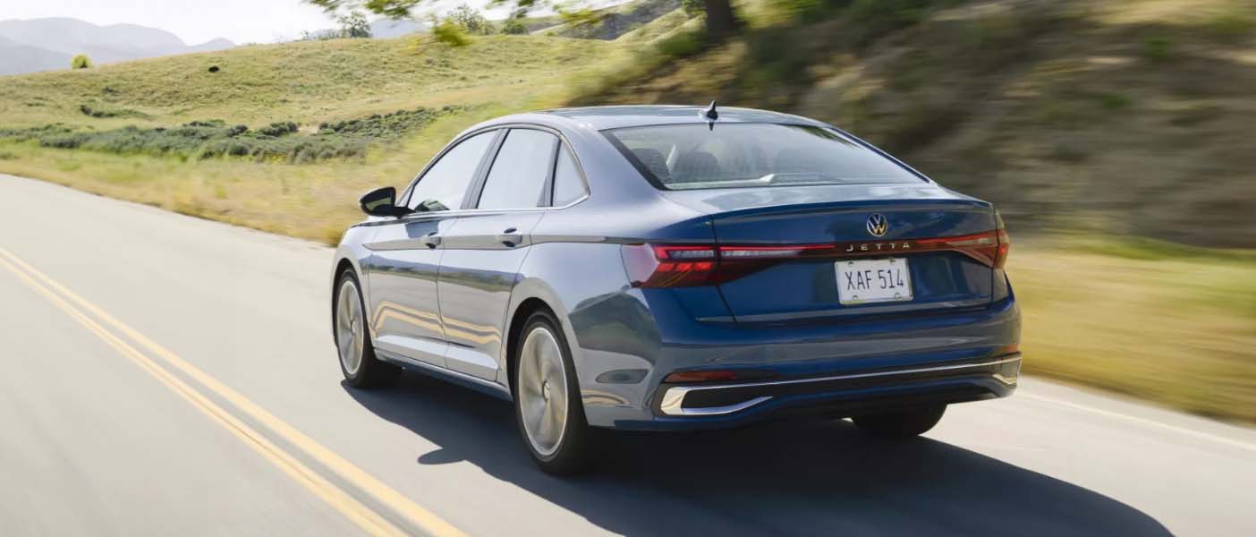 Rear view of Blue 2025 Volkswagen Jetta driving down the road
