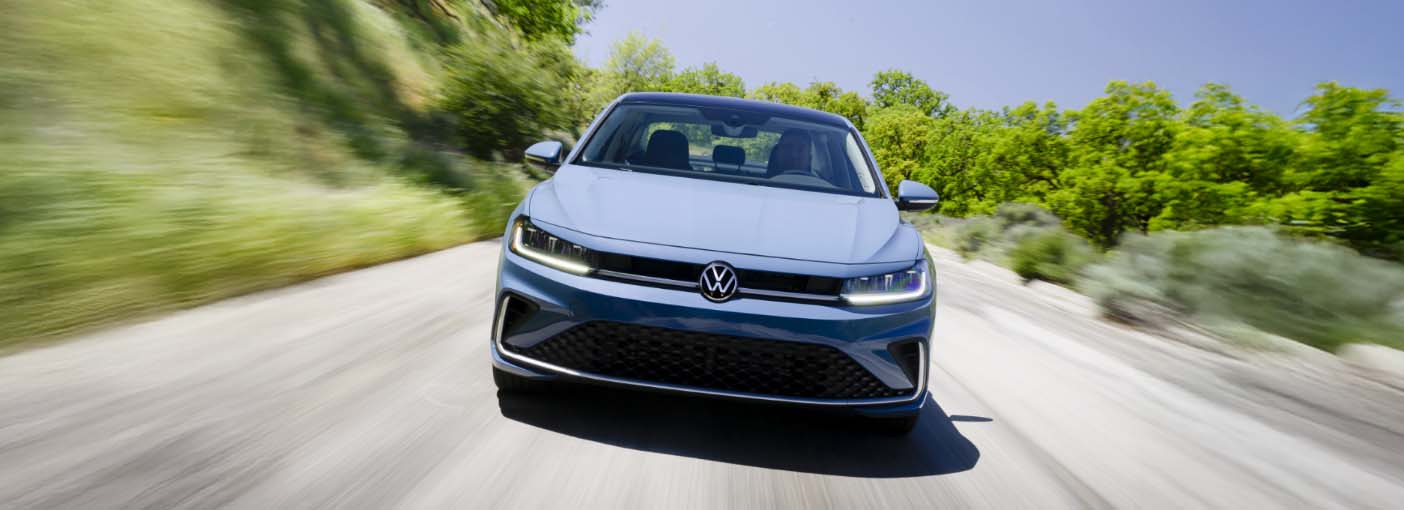 Front view of the blue  Volkswagen Jetta driving on a scenic road with greenery on both sides.