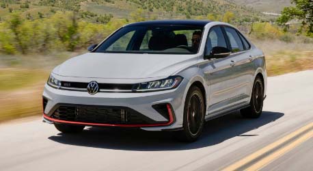 White_jetta_vw_gli_driving_on_road_near_green_hills