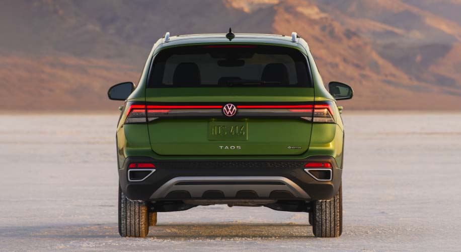 Rear view of a green 2026 Volkswagen Taos parked on a dirt road overlooking a mountainous landscape.