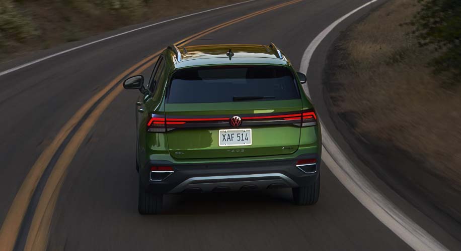 Rear view of the 2026 Volkswagen Taos in green driving through a winding forest road.