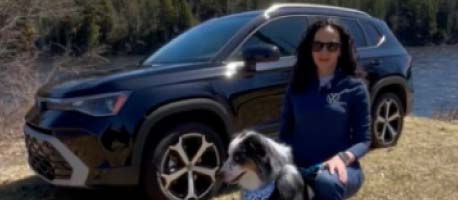 Woman with her dog sitting in front of a parked Volkswagen Taos