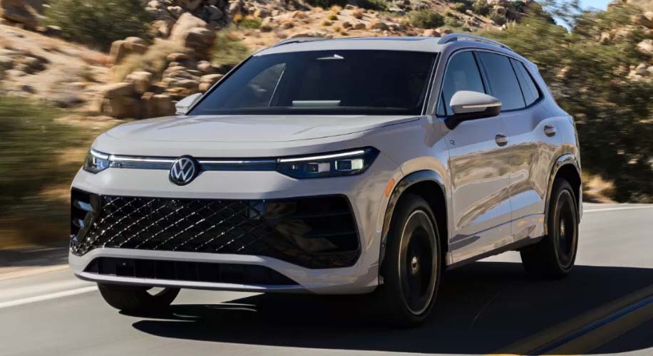 A light colored 2025 volkswagen tiguan SUV drives along a winding road through a mountainous landscape