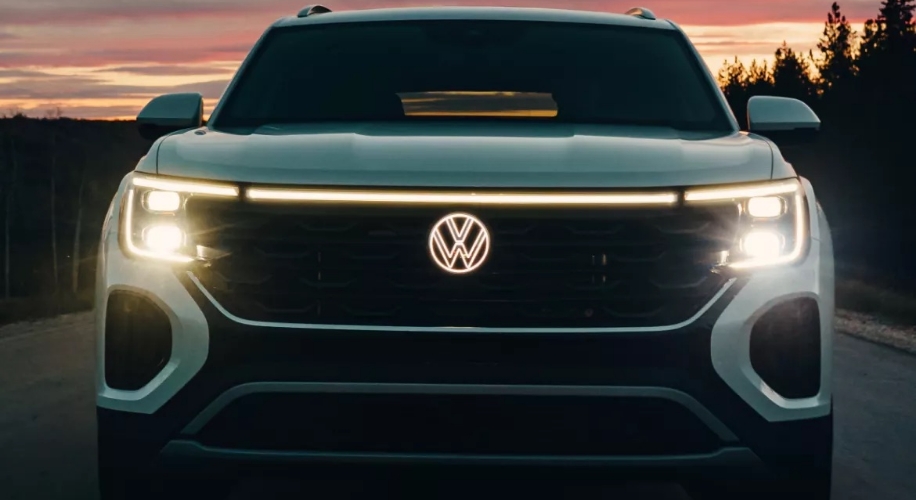 A front view of the Atlas Cross Sport with its headlights illuminated, stands out against a vibrant twilight sky painted with hues of pink and orange.