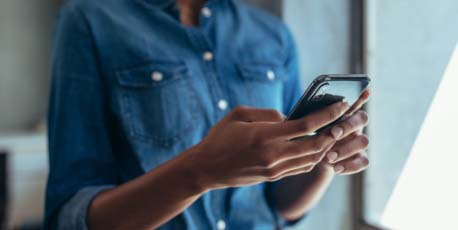 person_using_smartphone_near_window_wearing_denim_shirt_during_daylight