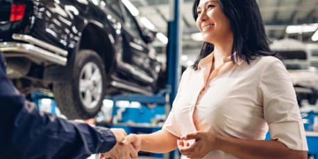 woman_smiling_and_shaking_hands_with_mechanic_in_auto_service_center_with_vehicle_on_lift_in_background