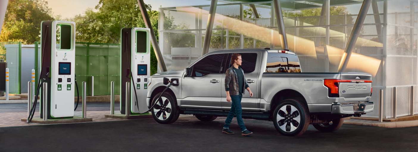 Man walking in front of a F150 Lightning at a public charging station.